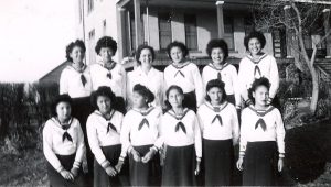 由12名身穿训练校服的加拿大女孩组成组,站在FileHills寄宿学校前拍相