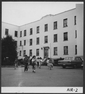 一群儿童穿过路前Alberni寄宿学校,一些汽车停在楼前